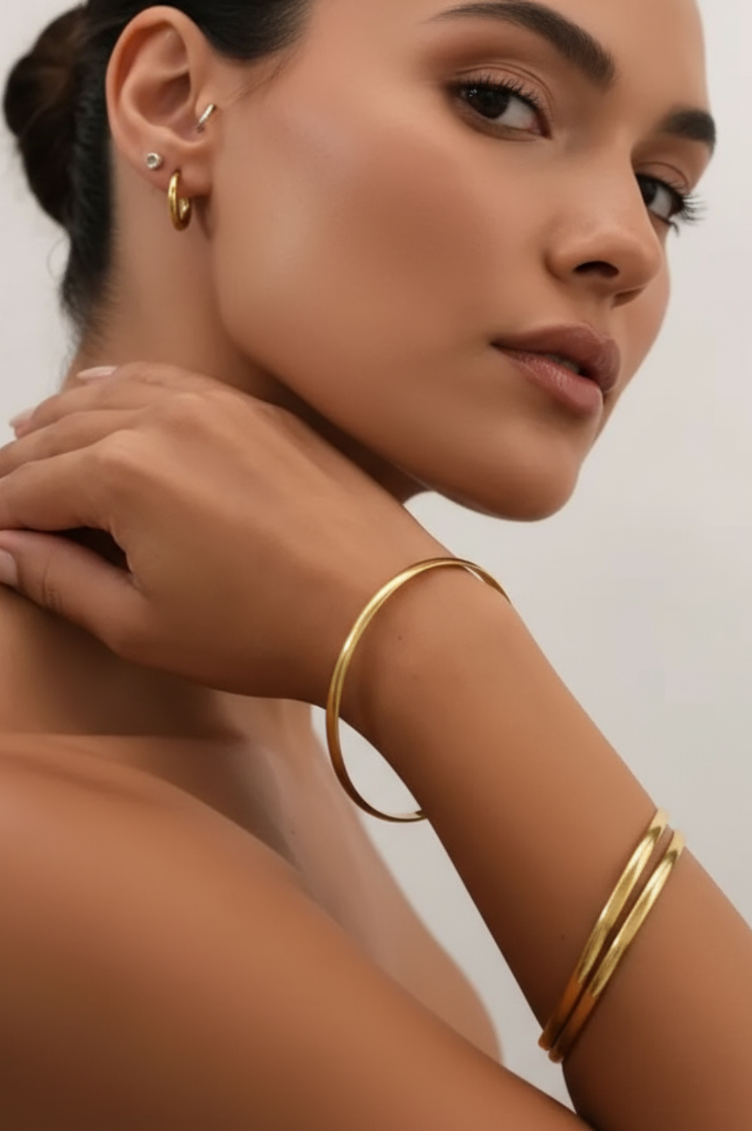 Woman wearing gold hoop earrings and bracelets on a neutral background