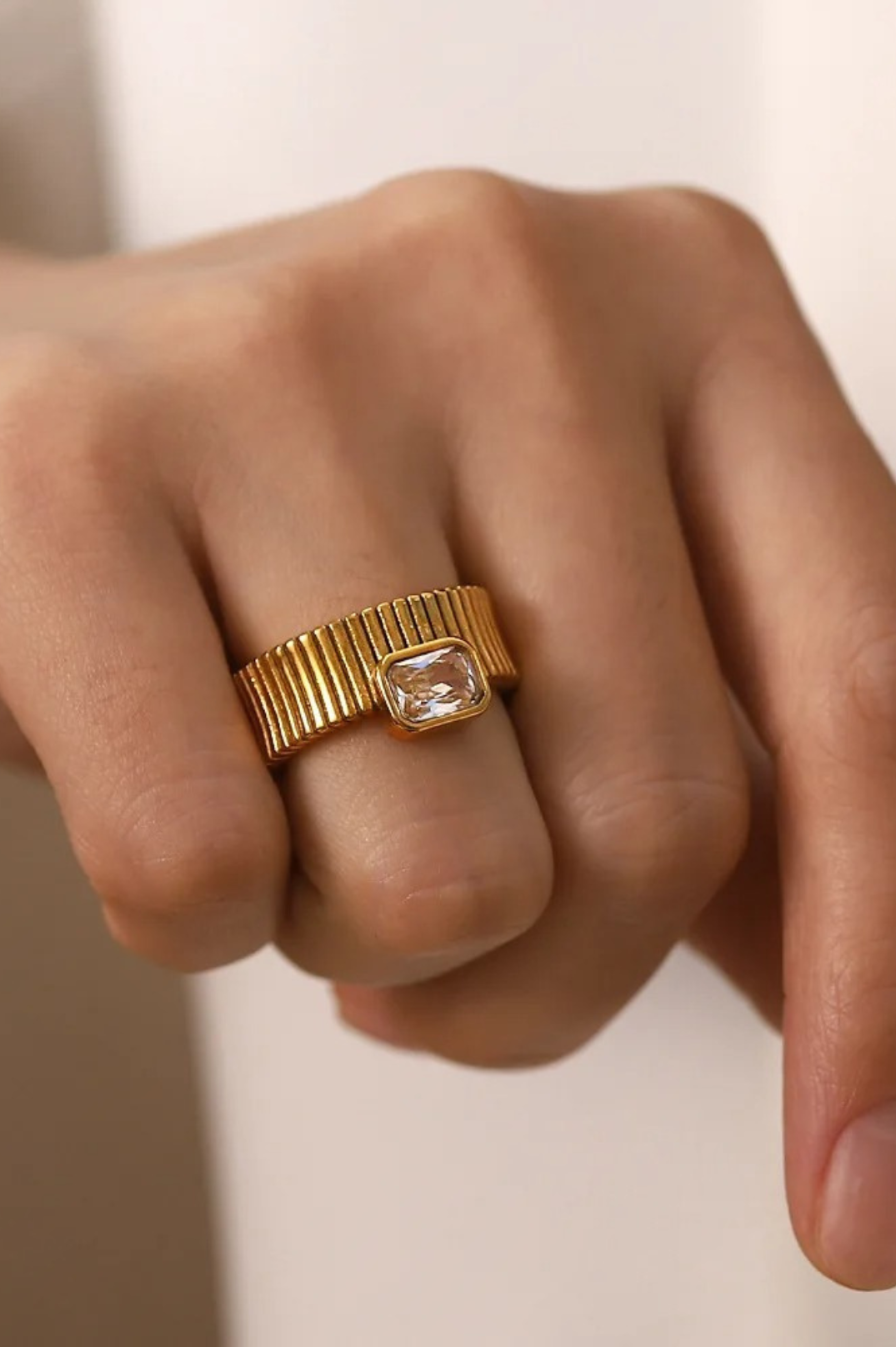 Gold ring with a diamond on a person's finger against a neutral background