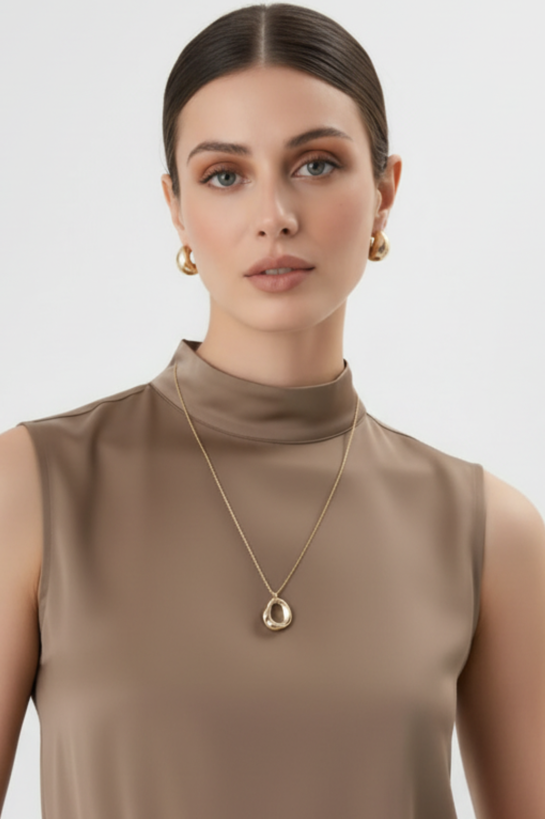 Woman wearing a gold necklace with a pendant against a light background