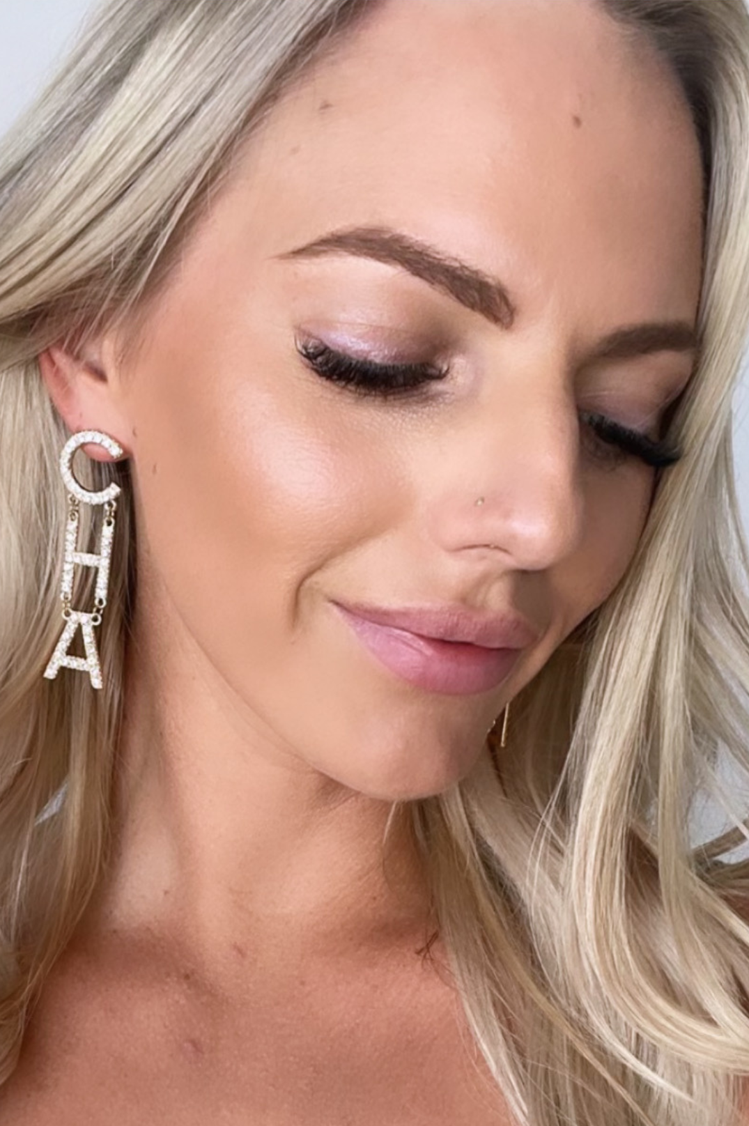 A close-up image of a woman's ear wearing a gold-colored earring with the letters 'CH' in a bezel setting.