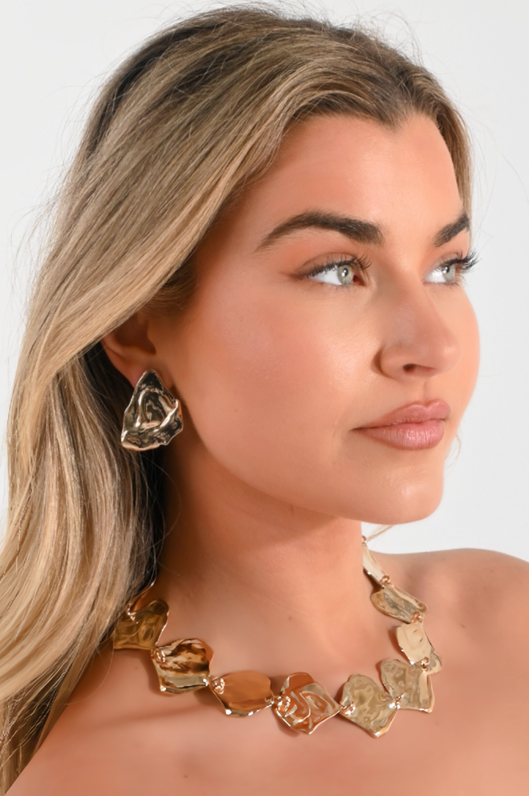 Woman wearing a gold necklace and earrings on a white background