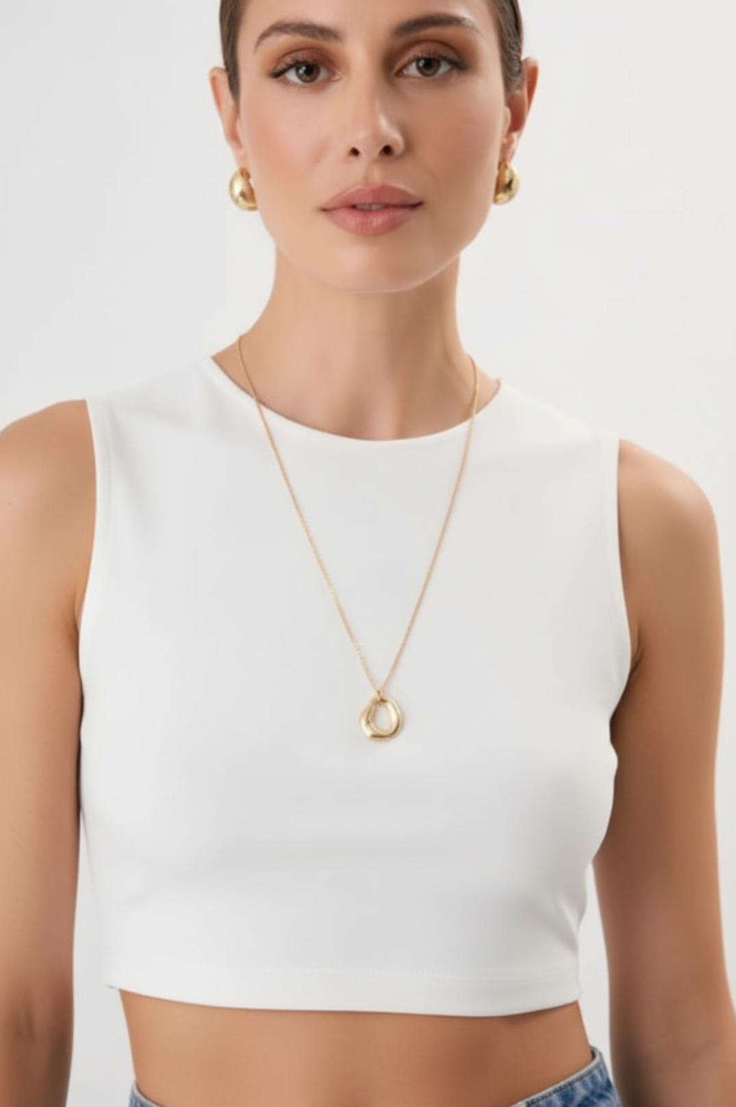 Woman wearing a white sleeveless top and gold necklace on a plain background