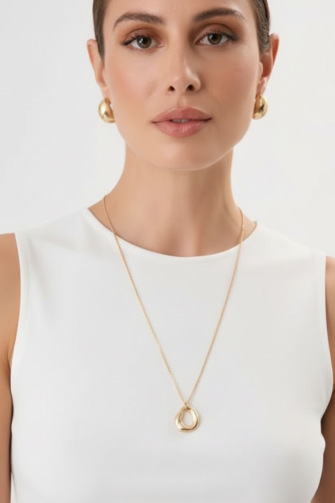 Woman wearing a gold necklace and earrings on a white background